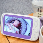 A parent sat on the couch looking at the baby monitor while having a cup of tea.