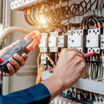 Electrician engineer uses a multimeter to test the electrical installation and power line current in an electrical system control cabinet.